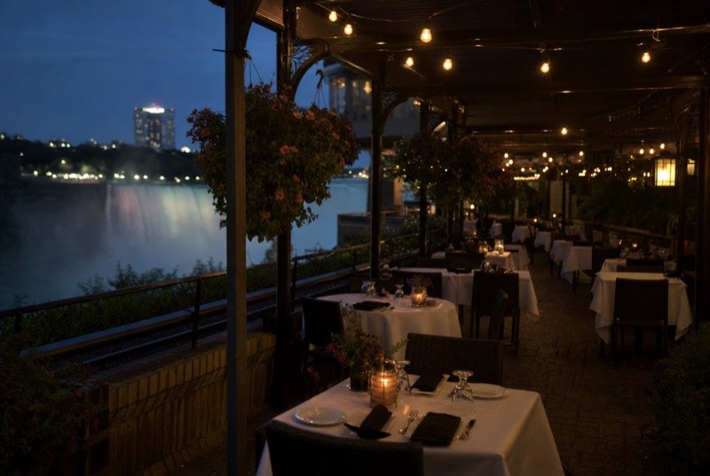 An empty restaurant patio with laid tables under warm string lights at dusk